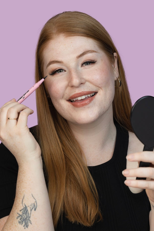 A model smiling and applying adhesive eyeliner used to glue on fake eyelashes.